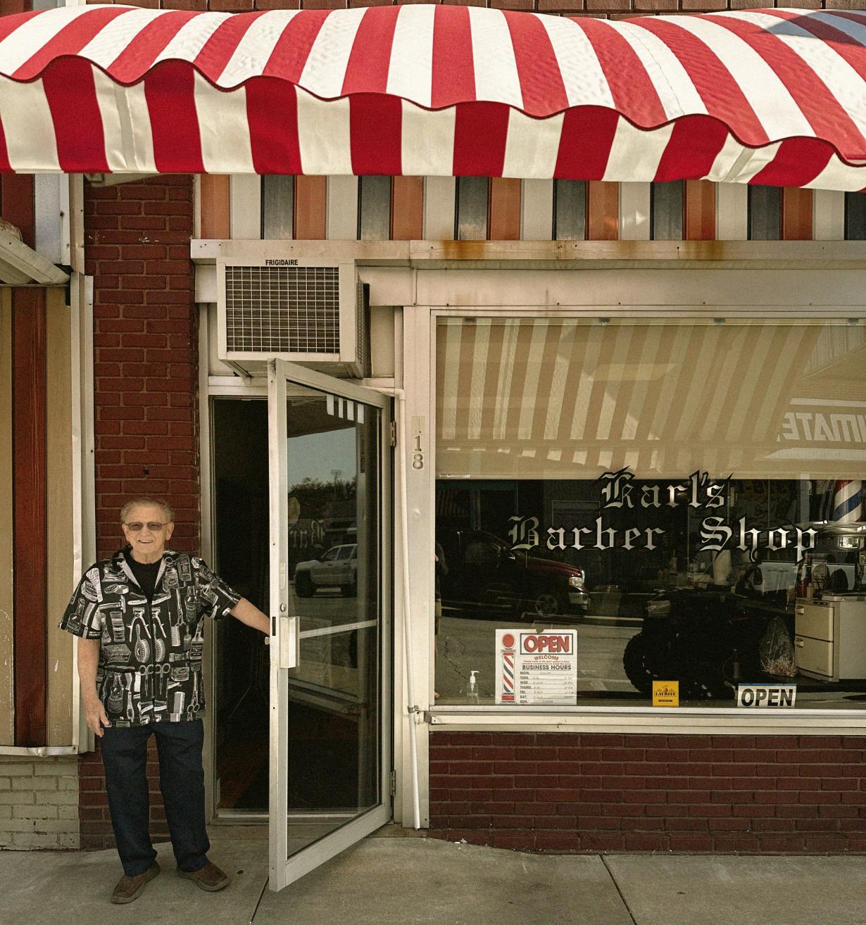 A photograph of Karl standing in front of the barber shop.